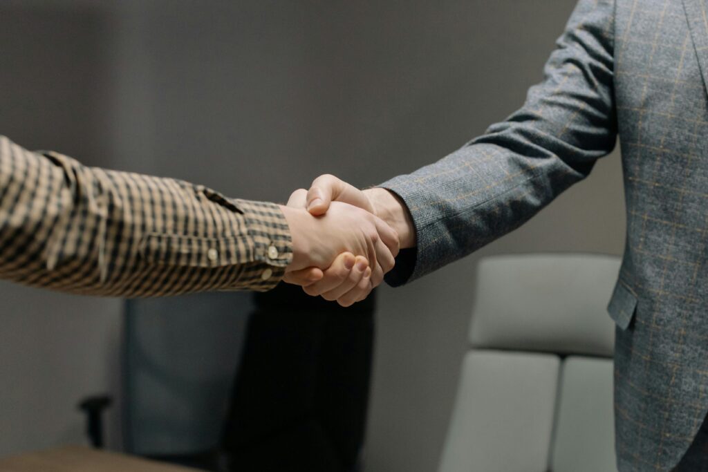 Hakkımızda 1 Close-up of two professionals shaking hands in an office, symbolizing successful business dealings.